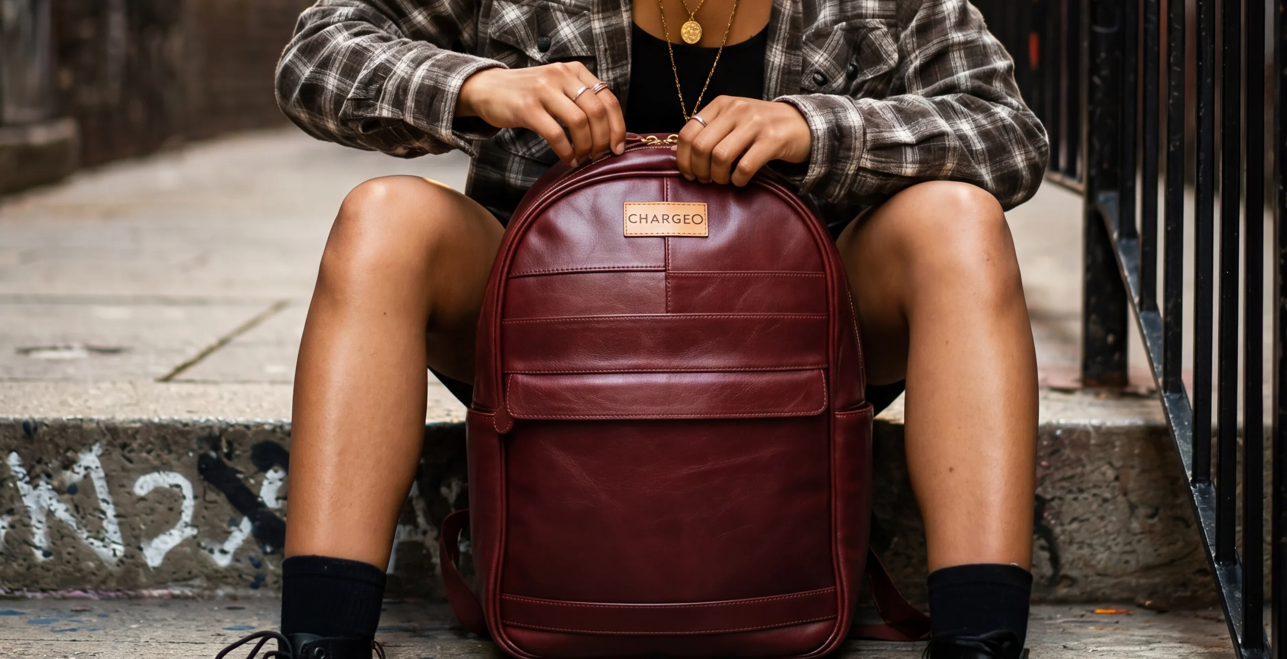 Hands opening a CHARGEO burgundy leather backpack, with the CHARGEO mark on the front