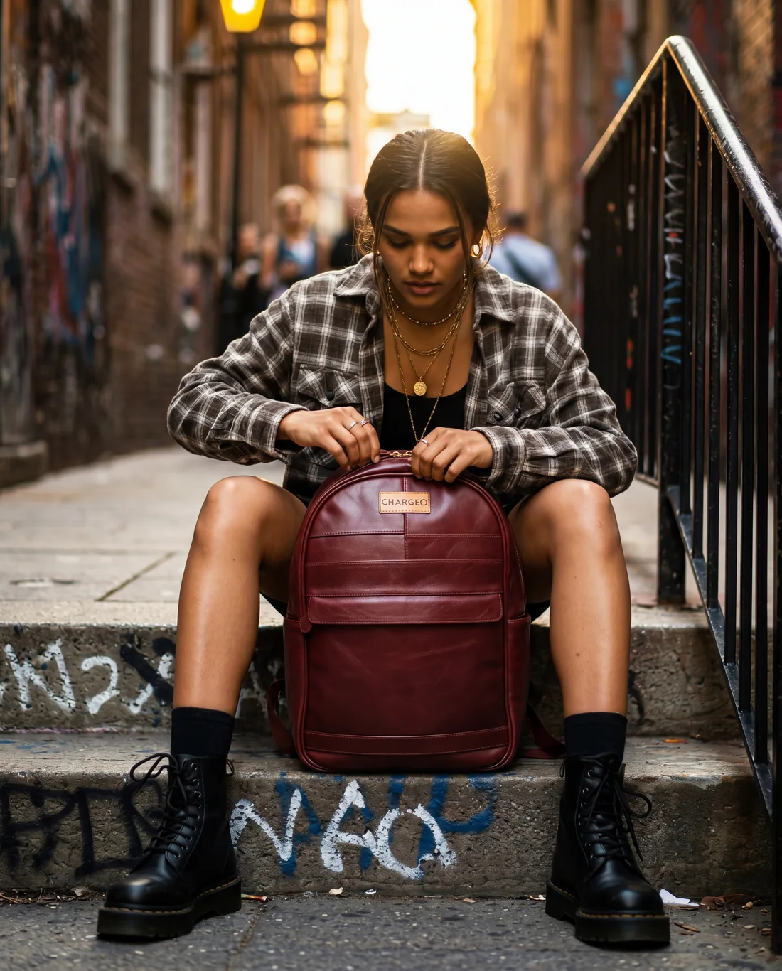 Woman seated on city steps opening a CHARGEO burgundy leather backpack