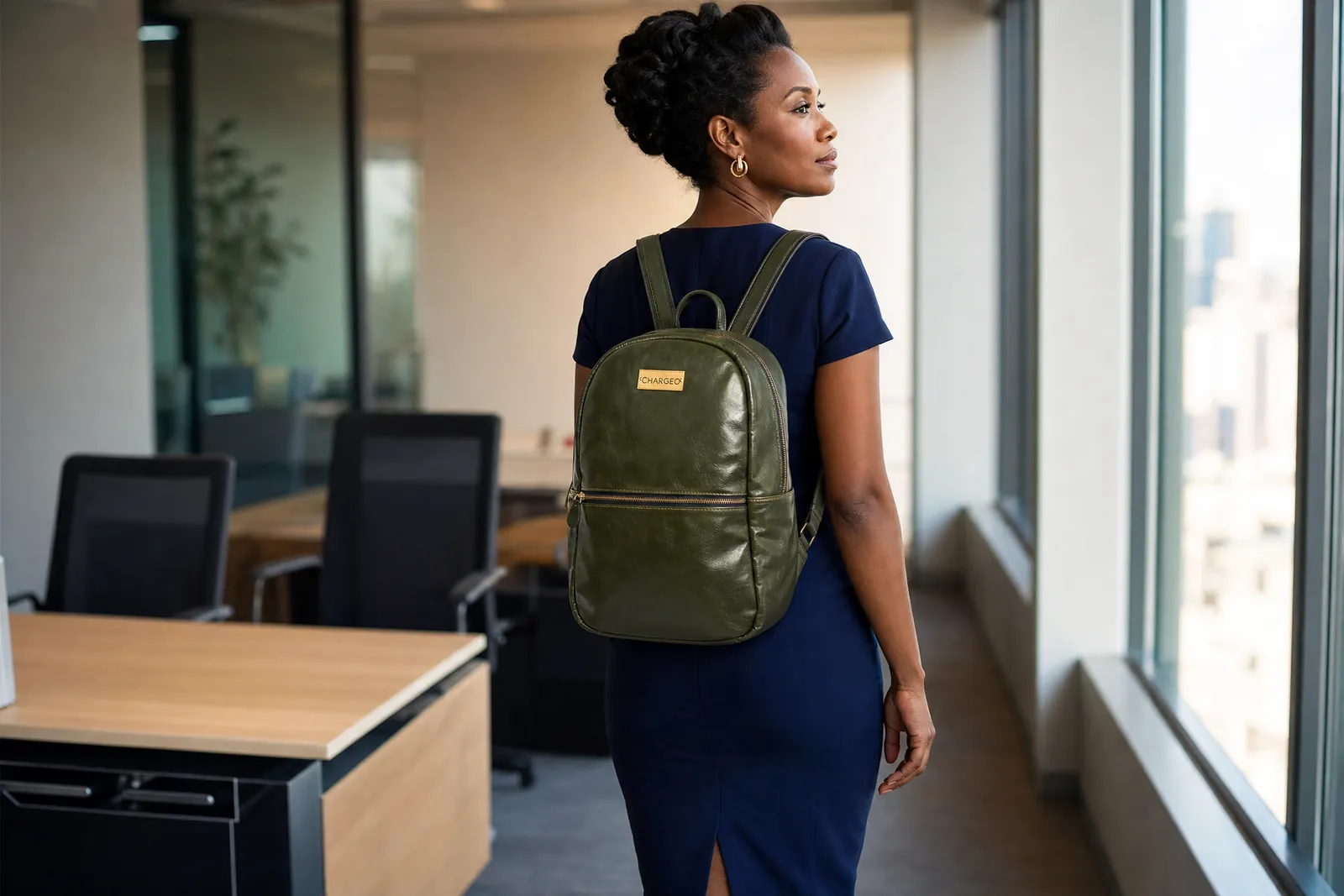 Woman in a navy dress in an open office wearing a CHARGEO Fourways Leather Backpack for Women