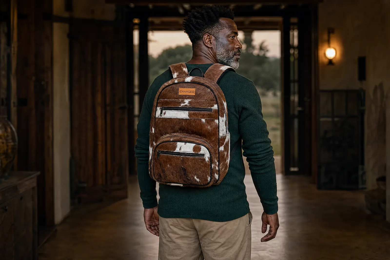 Man in a farmhouse hallway wearing a CHARGEO Zulu Treasure Nguni hide leather backpack