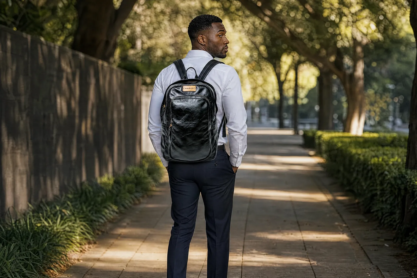 Man on a tree-lined street in Rosebank wearing a CHARGEO charcoal leather backpack
