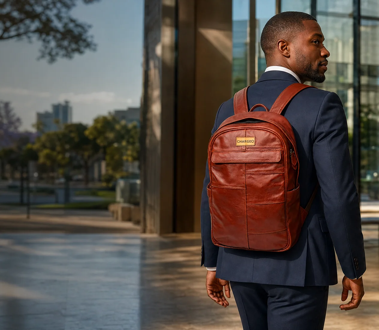 Man in a navy suit walking into an office reception in Rosebank wearing the CHARGEO Stellenbosch Leather Backpack in Cognac on both shoulders