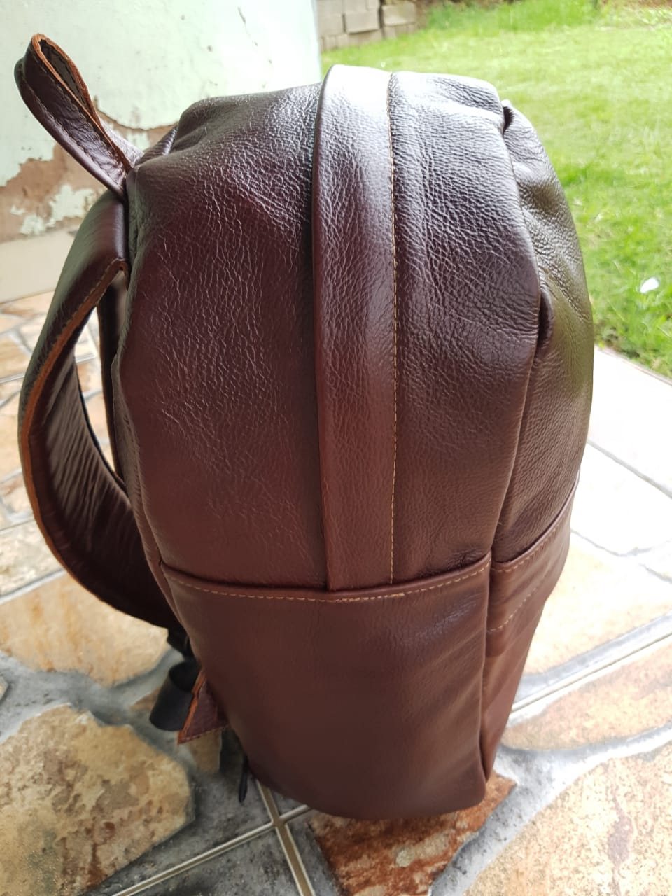 Thabani Mngadi's first leather backpack, oxblood, standing on grass