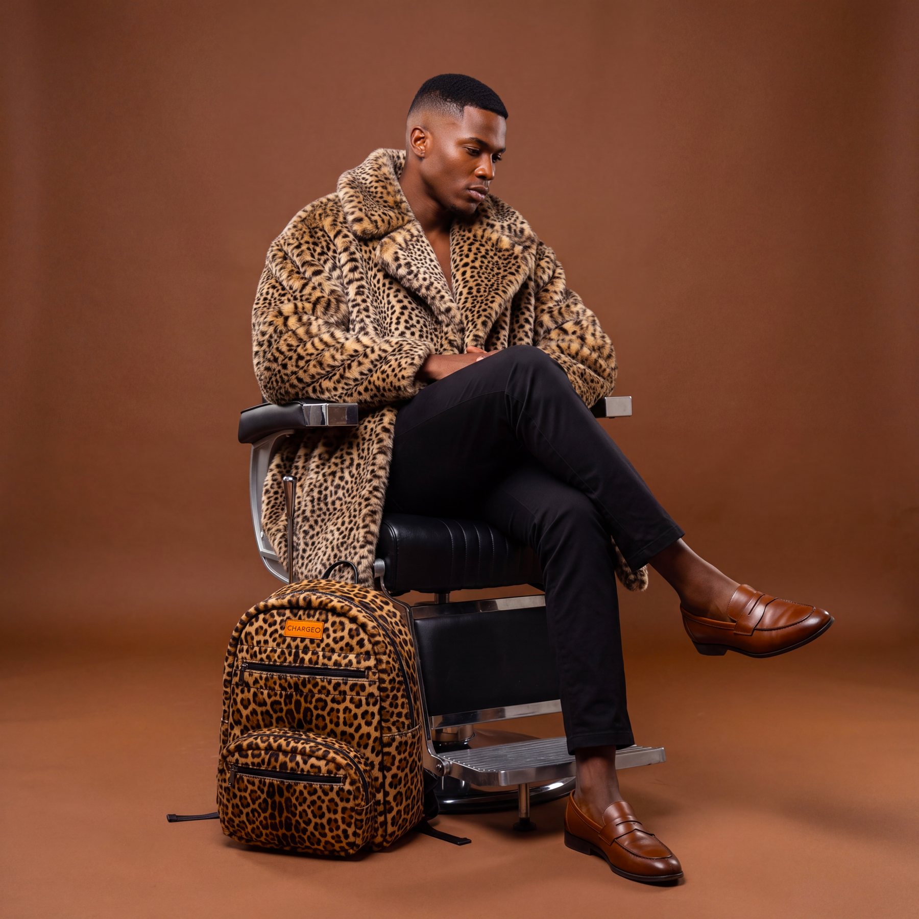 A man in a leopard print coat seated beside a CHARGEO Zulu Treasure Leather Backpack